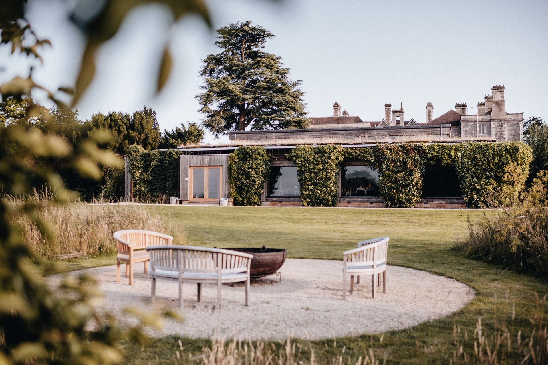 The ivy-covered Gillyflower building seen across the lawn from a fire pit ringed with wooden benches.