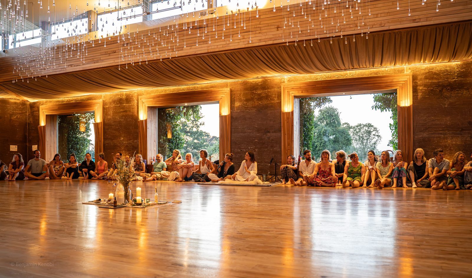 Dancers sit barefoot around the edge of a candlelit wooden floor in the Gillyflower, with crystal lights above and gardens through the windows.